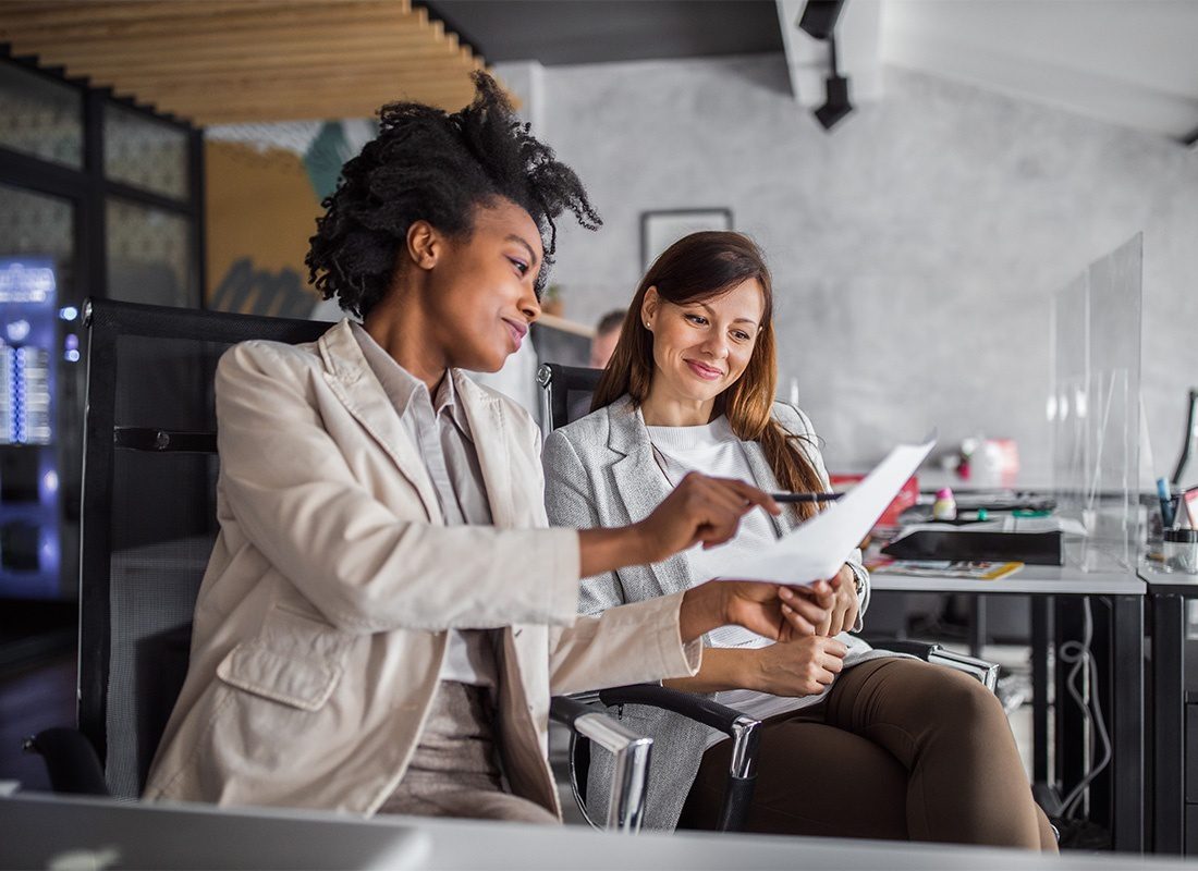 Payroll HRIS Applicant Tracking and PEO Due Dilligence - Smiling Young Business Woman Showing her Female Colleague a Document in the Office