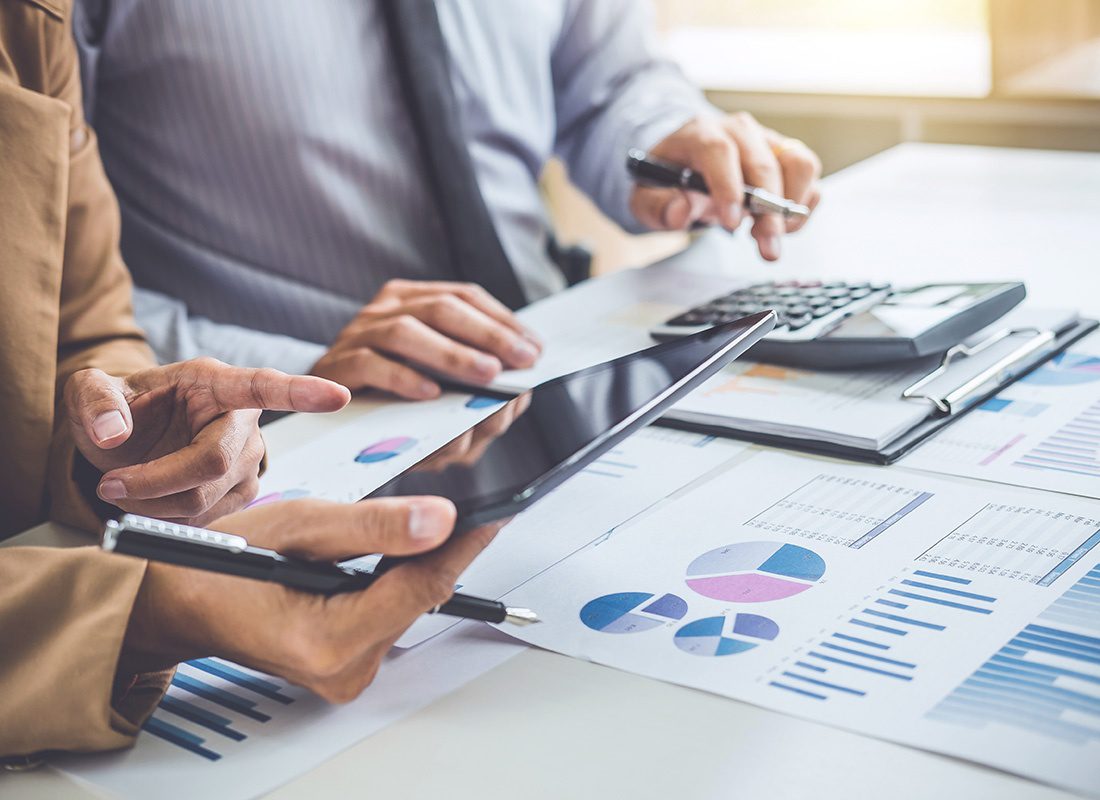 Transaction Advisory Services - Closeup View of a Business Man and Woman Working Together on Financial Data Analysis with a Calculator Tablet and Numerous Data Charts in the Office